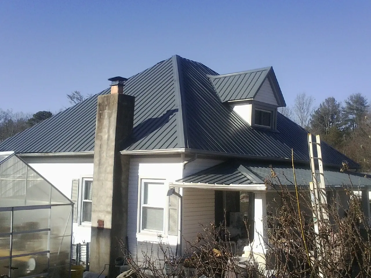 Dark blue standing seam metal roof on a white farmhouse with dormer — Slate & Tile Roof Repair by Roofing Brothers in Roopville