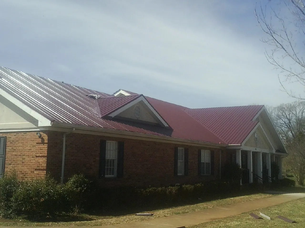 Red metal roof with gabled entries on a long brick building, from a Hail Damage Roof Repair job in Roopville