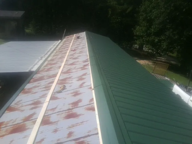 Old rusted panels beside newly installed green metal roofing — Wind Damage Roof Repair by Roofing Brothers in Roopville