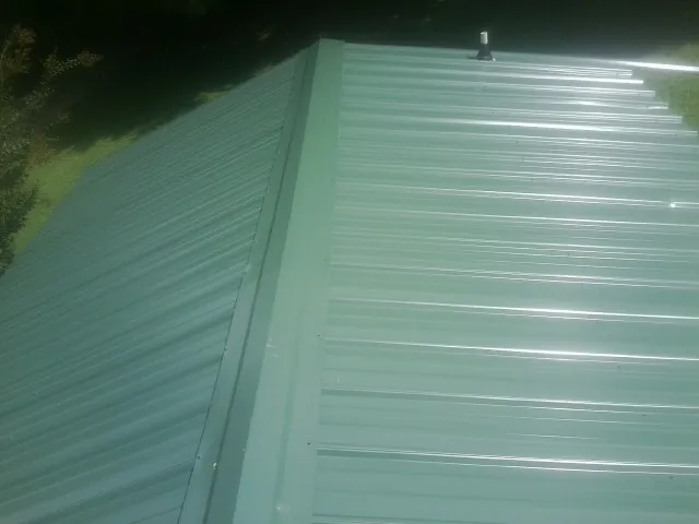 New green metal panels meeting at the ridge of a roof — Flat Roof Repair work by our crew in Roopville