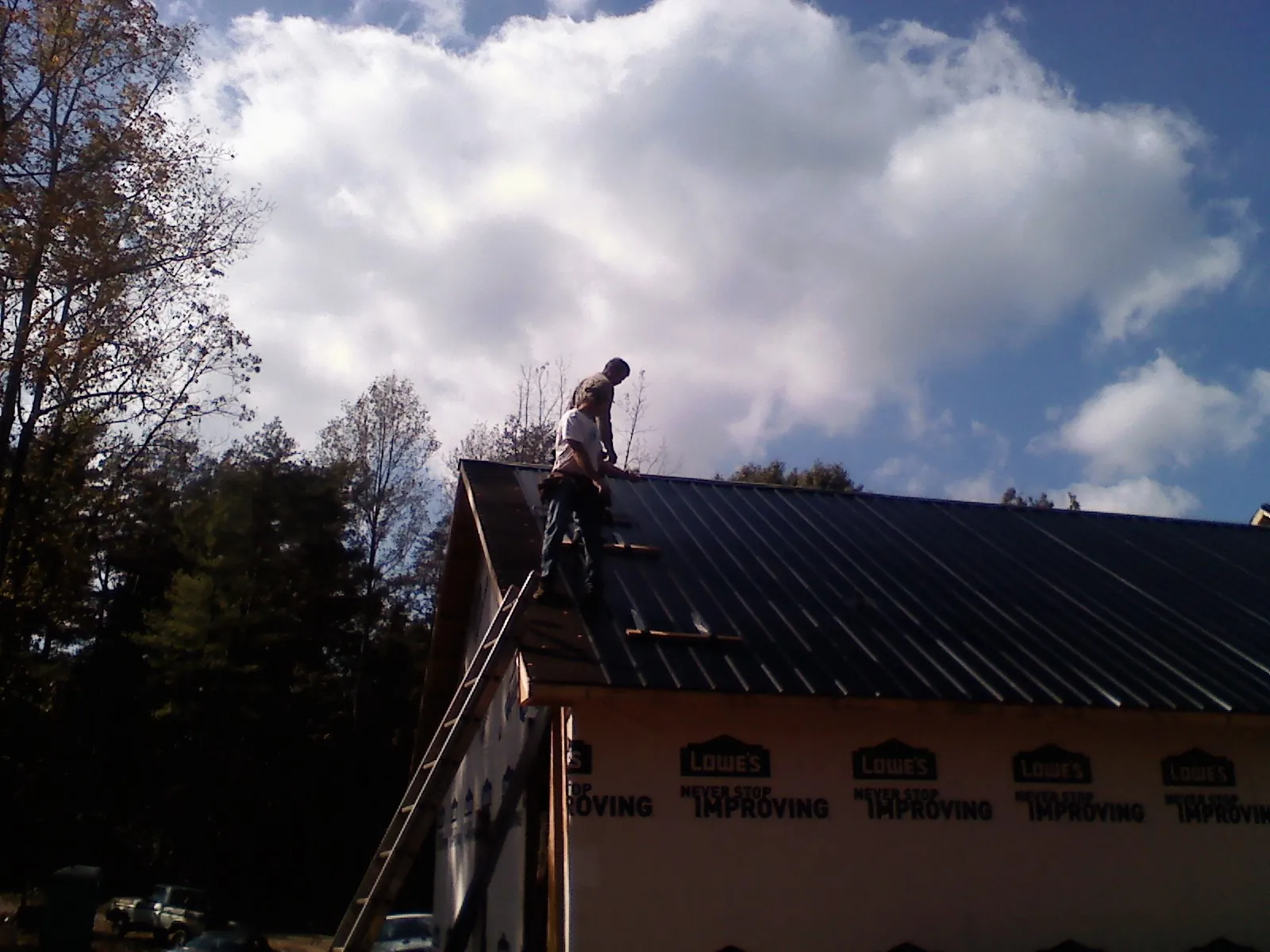 Roofer fastening dark metal panels high against a cloudy sky, from a Roof Inspection job in Roopville