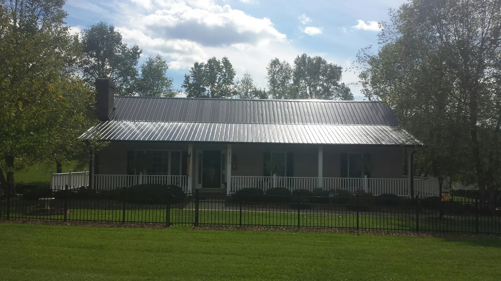 Gray metal roof on a brick ranch with a full width front porch — Gutter Guard Installation work by our crew in Roopville