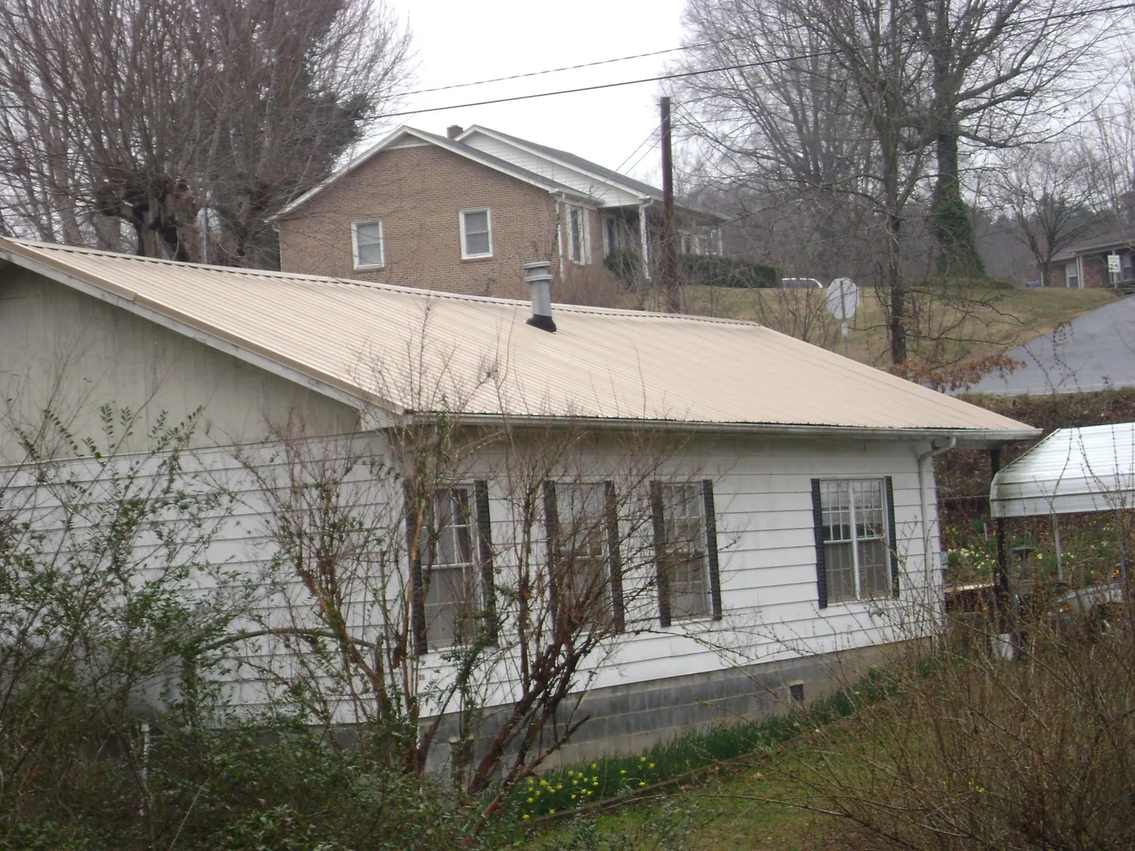 Tan metal roof on a white sided house set into a hillside — Commercial Roofing by Roofing Brothers in Roopville